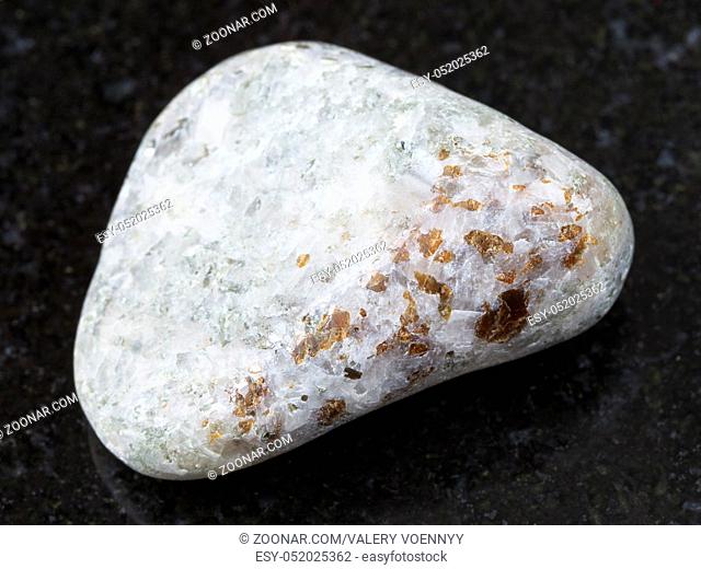 macro shooting of natural mineral rock specimen - brown chondrodite crystals in tumbled calcite stone on dark granite background from Pitkyaranta region of...