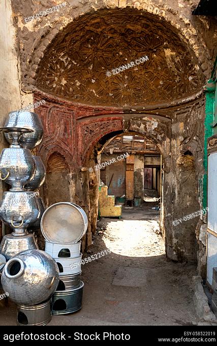 Arched passage between shabby houses with Egyptian traditional aluminum utensils stacked by wall in old Cairo city, Egypt on daytime