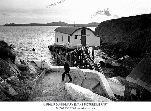 A crewman climbs the steps from the RNLI St Davids lifeboat station at St Justinian, Pembrokeshire, South Wales. The previous lifeboat station can be seen...