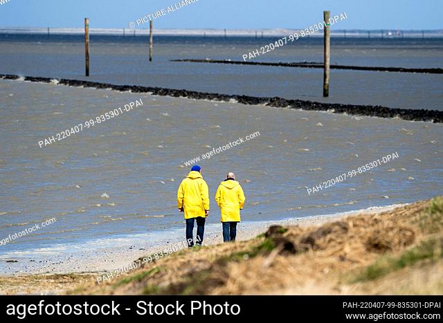 07 April 2022, Lower Saxony, Harlesiel: Tourists walk along the beach in stormy weather and look out over the North Sea. The German Weather Service (DWD) warns...