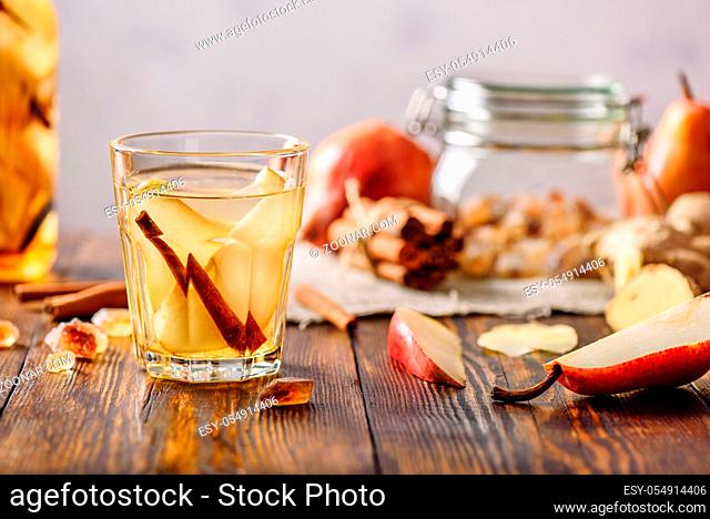 Glass of Water Infused with Sliced Pear, Cinnamon Stick, Ginger Root and Some Sugar. Ingredients Scattered on Wooden Table