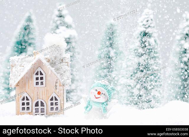 Small decorative snowman near wooden house in fir forest under falling snow