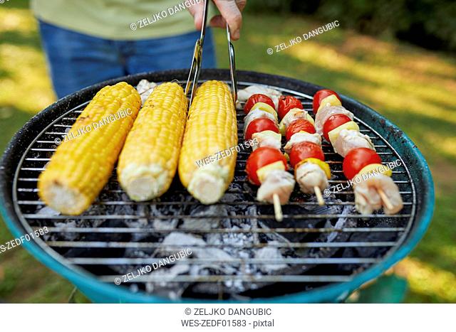 Corn cob and meat skewer on grill at barbecue in garden