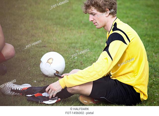 Young soccer player holding mobile phone while sitting on field