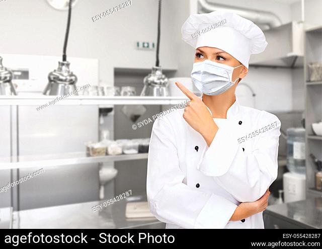 female chef in mask pointing finger up at kitchen