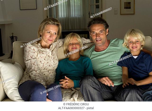 Family sitting together on sofa, watching TV
