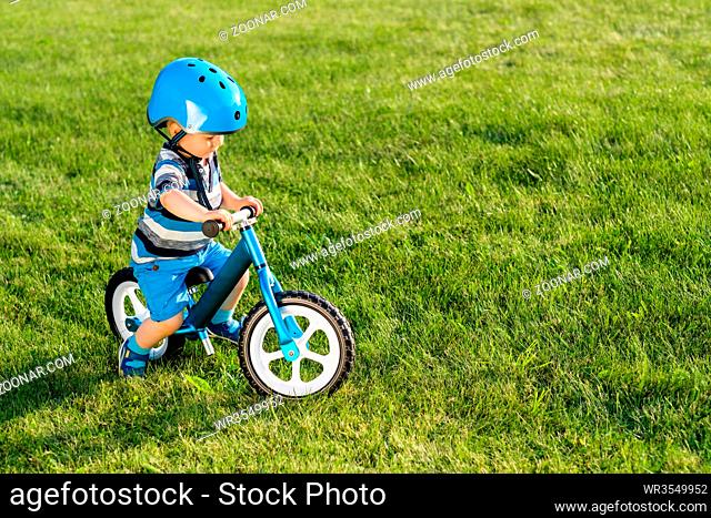 Boy in helmet riding a blue balance bike (run bike). Happy child learning to keep balance on a training bicycle in the garden