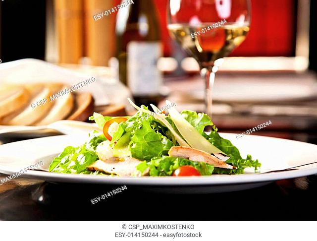 Chicken salad with vegetables and croutons, bottle of wine on the background