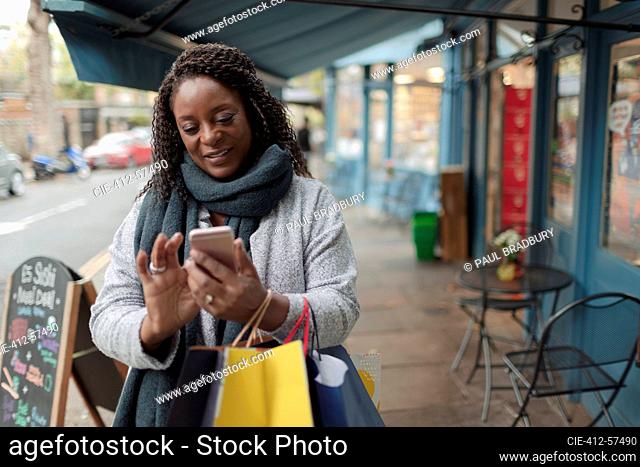 Mujer con teléfonos inteligentes y bolsas de compras en la acera
