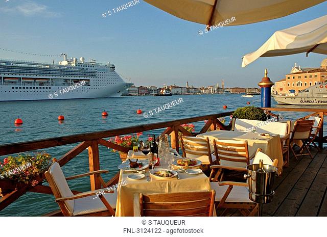Tables and chairs on the Hotel Cipriani terrace, cruise ship passing by, Giudecca, Venice, Italy