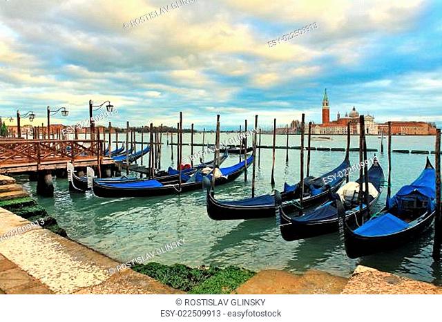 Gondolas moored in a row at wooden pier on Grand Canal against background of San Giorgio Maggiore church in Venice, Italy
