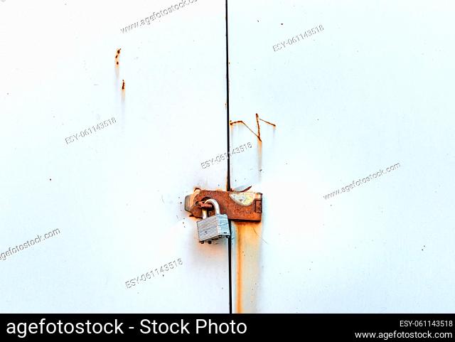 Locked simple metal padlock hanging on rusted hasp on plain metal doors of garden shed