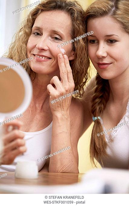 Mother applying face cream on her face while daughter looking