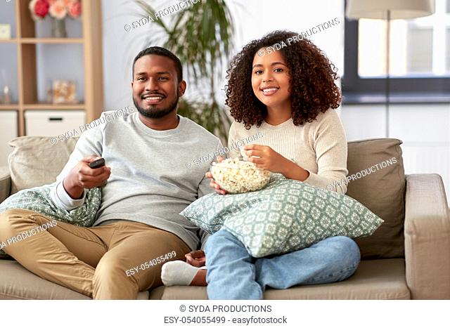 african couple with popcorn watching tv at home
