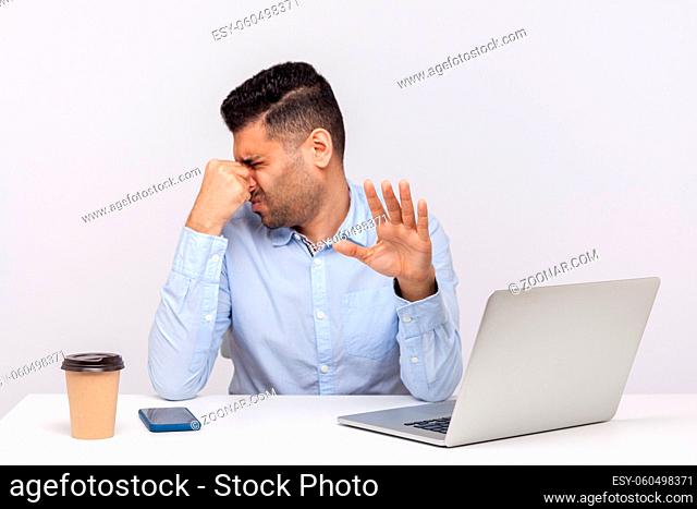 Displeased male employee confused by bad smell in office workplace, holding breath pinching his nose to avoid awful stink, showing stop gesture