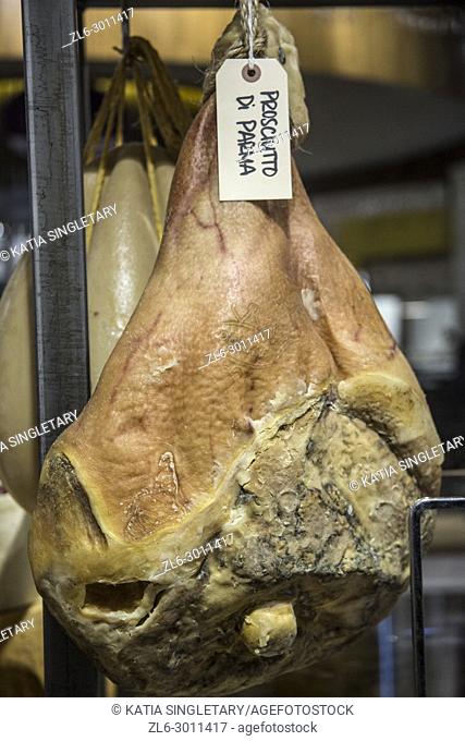 A whole leg of Italian ham, of prosciutto di parma hanging by a hook in an indoor market