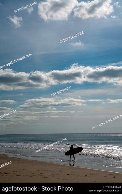 A male surfer walks into the Atlantic ocean on the French Cote d'Argent to catch some waves