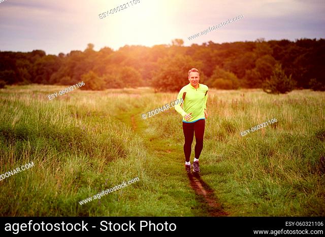Fit muscular man jogging on a rural trail at sunset through grassland wearing sportswear in an active lifestyle concept