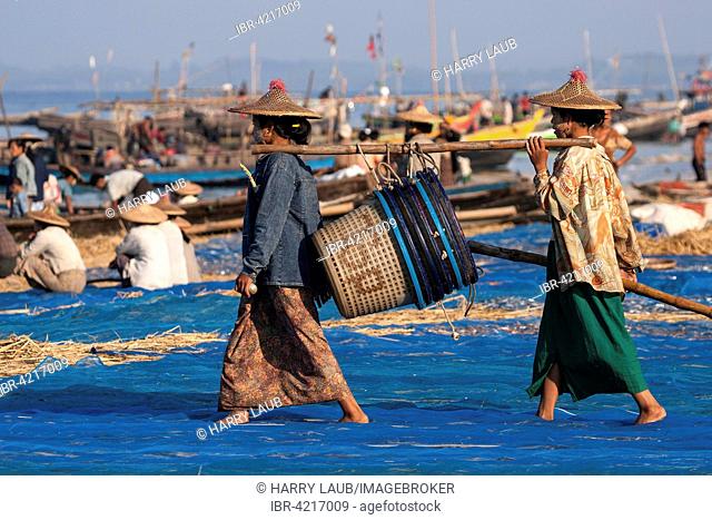 Local women wearing a straw hat, carrying empty fish baskets to the sea, behind fishing boats on the beach of the fishing village Ngapali, Thandwe