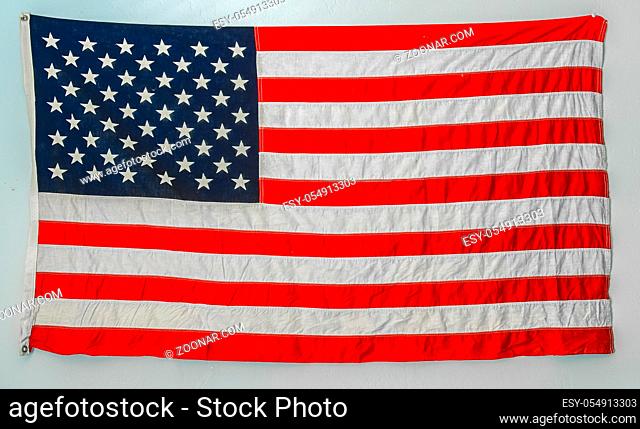 Worn american flag hanging from wall on a blank white wall