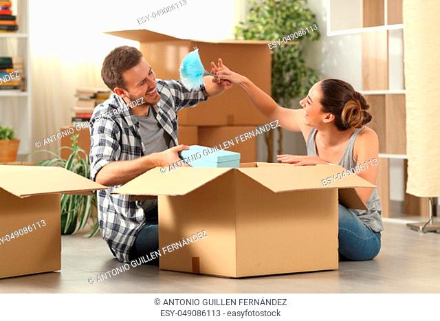 Happy couple joking moving home boxing belongings sitting on the floor in the night