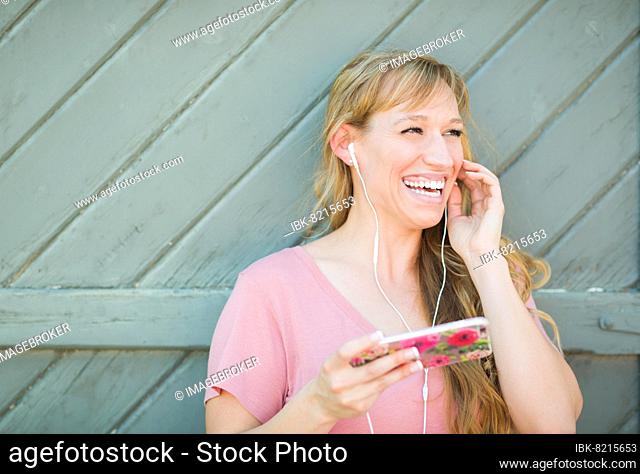 Outdoor portrait of young adult brown eyed woman listening to music with earphones on her smart phone