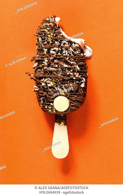 A chocolate bar isolotated on an orange background, drizled with toppings and more chocolate