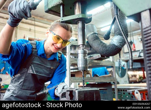 Woman worker in metal workshop using pedestal drill to work on piece