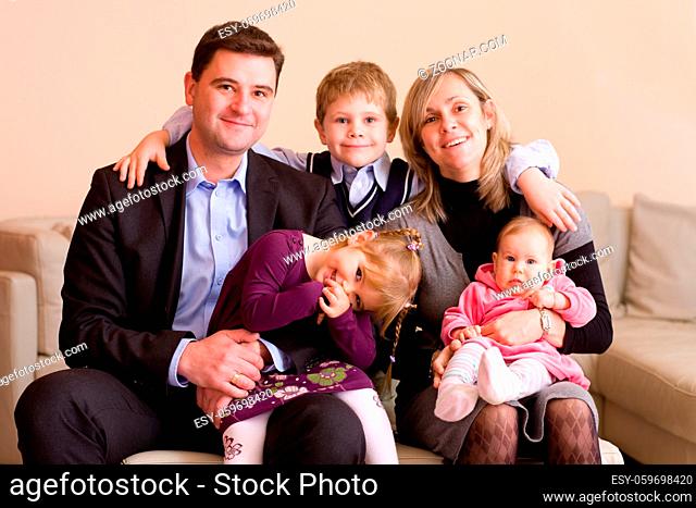 Portrait of happy family sitting on couch at home, smiling: father, mother, son, younger sister and a baby girl