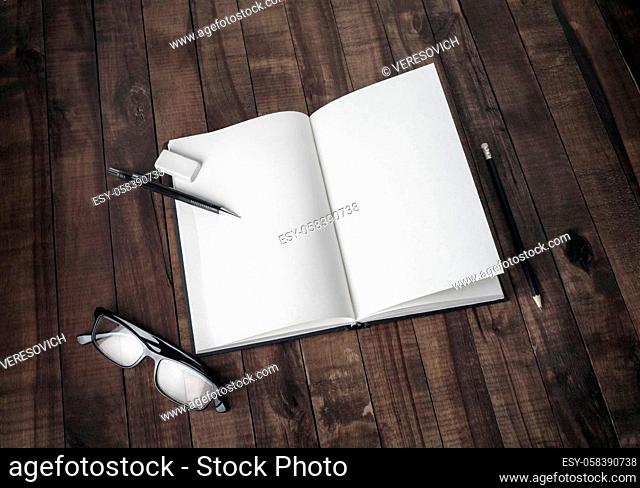 Mockup of opened blank brochure, pencil, glasses and eraser on wood table background. Stationery mock up. Responsive design template