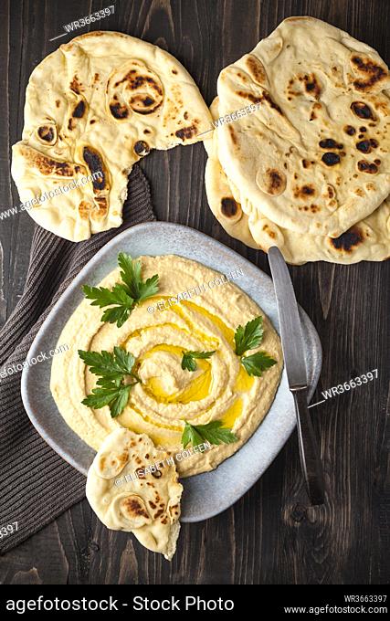 Plate of hummus with flat breads on wooden table, close up