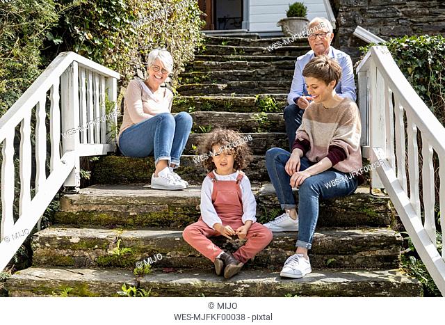 Senior couple with adult daughter and grandson sitting on stairs in garden of their home