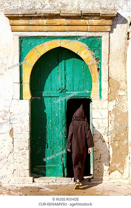 Rear view of man wearing traditional clothing stepping into door, Essaouira, Morocco