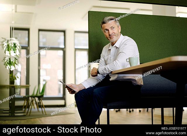 Smiling man looking away while using digital tablet at cafeteria in office