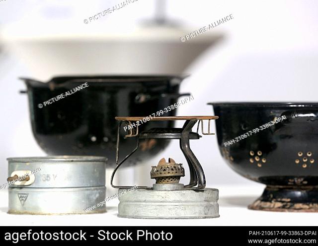 17 June 2021, North Rhine-Westphalia, Duesseldorf: A small electric cooker (l) and an alcohol stove, both made from gas mask parts (front) and a cooking pot (l)...
