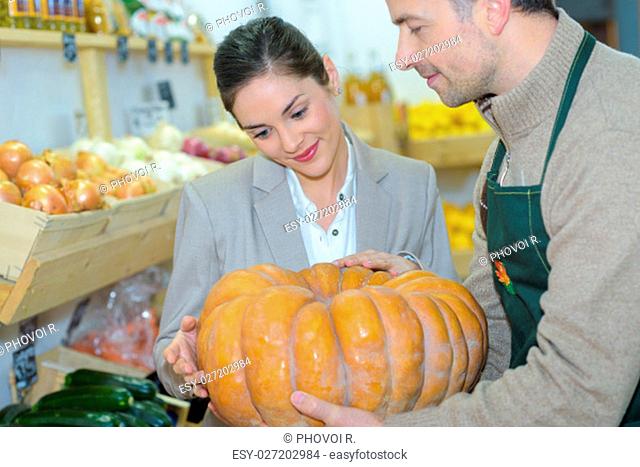 Grocer showing pumpkin to customer