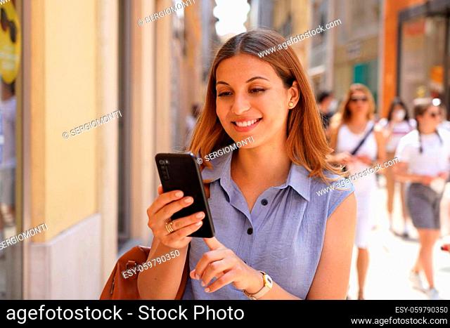 Portrait of smiling young woman using smartphone in the street with people walking on the background