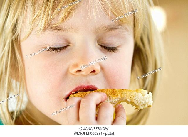 Portrait of little girl eating with closed eyes
