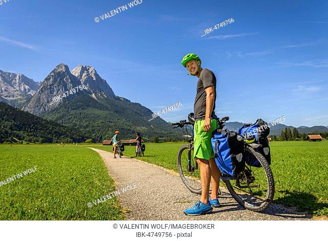 Cyclist on bike tour stands on bike path next to his mountain bike, in the back Zugspitze, Tegernauweg, near Grainau, crossing the Alps, Garmisch-Partenkirchen