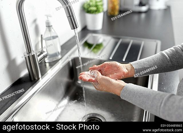 woman washing hands with liquid soap in kitchen