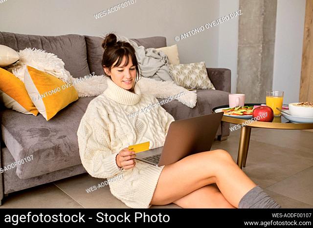 Smiling woman shopping online through laptop while sitting in living room at home
