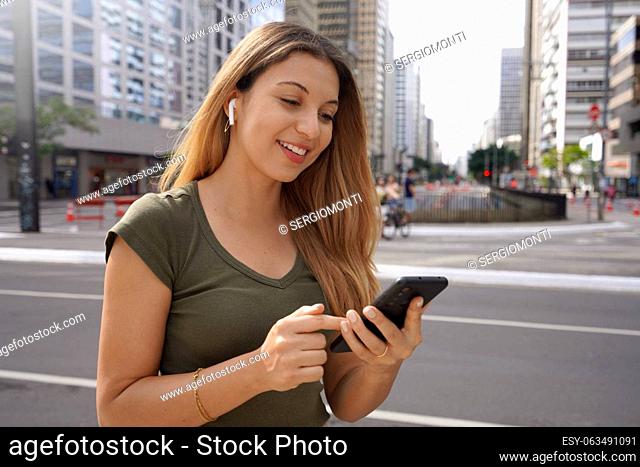 Smiling stylish girl reading a text message on her phone while commuting in the city