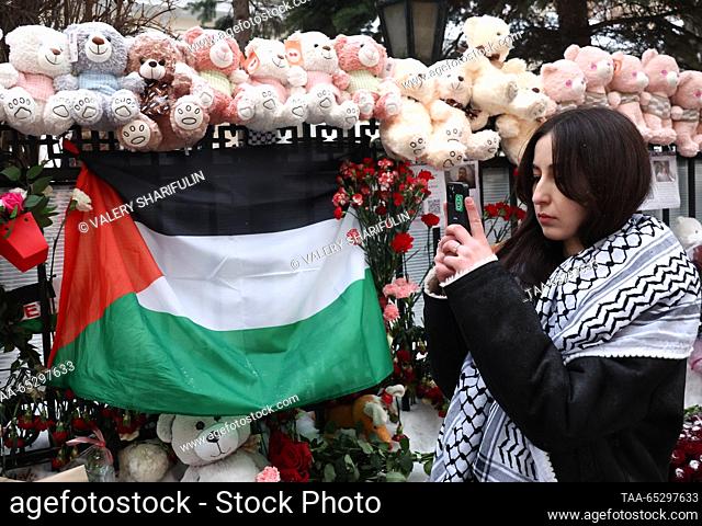 RUSSIA, MOSCOW - NOVEMBER 28, 2023: A woman wearing a Palestinian keffiyeh takes a photograph on her mobile phone in front of tributes for the victims of...