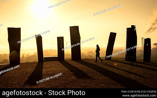 14 September 2021, Bremen: A woman walks across the Metalhenge viewpoint at the Blockland Landfill at sunrise. Photo: Sina Schuldt/dpa