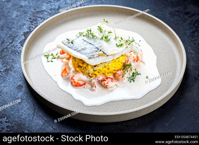 Fried haddock filet with saffron rice and shell prawns in crab sauce as closeup on a modern design plate