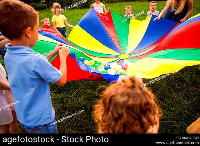 Intresting outdoors games for kids at summer. Multicolored rainbow parachute full of balls