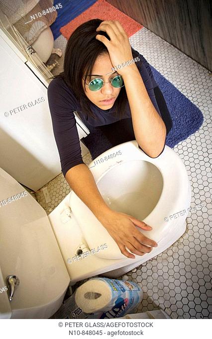 Young woman, wearing sunglasses, kneeling by her toilet