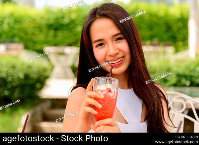 Portrait of young beautiful Asian woman relaxing at the coffee shop with nature outdoors
