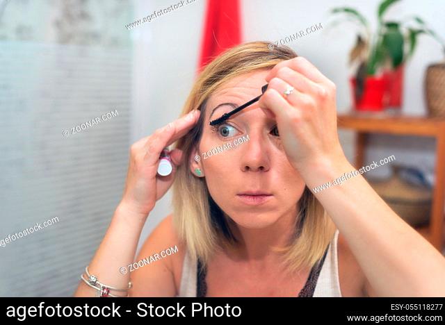 Beautiful blonde woman applying mascara on her eyelashes