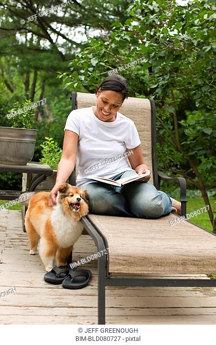 African American woman reading book and petting dog